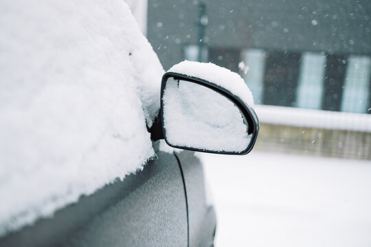 Close-up of a snow-covered wing mirror on a vehicle door after a heavy winter blizzard. Frozen automobile on outdoor parking lot, cold seasonal weather and transport concept.