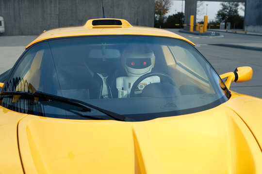 Robot driving a yellow futuristic autonomous car outdoors