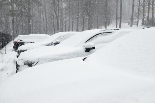 Parked vehicles buried under deep fresh snow during heavy blizzard in winter season. Automotive transport, cold weather conditions, and urban winter snowfall concept.