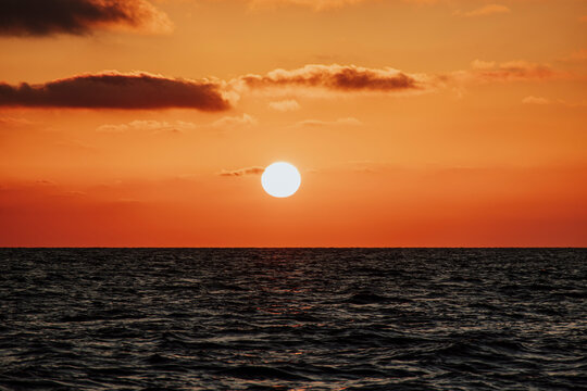 The bright sun sets over the calm ocean water