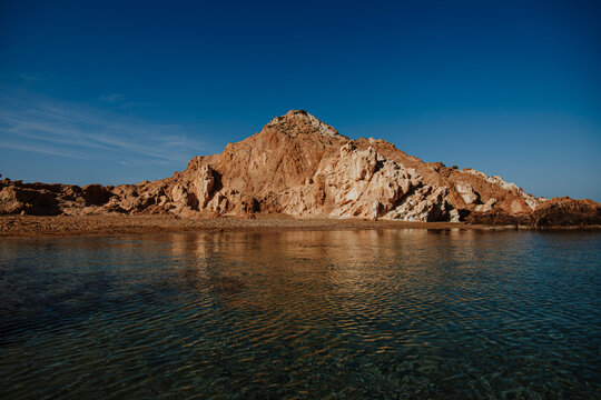 A rocky island sits in the crystal clear water of Cala Pregonda