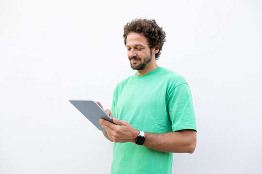 Smiling man in green shirt uses a tablet on a white background
