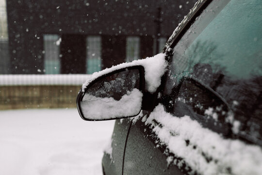 Close-up of a snow-covered wing mirror on a vehicle door after a heavy winter blizzard. Frozen automobile on outdoor parking lot, cold seasonal weather and transport concept.