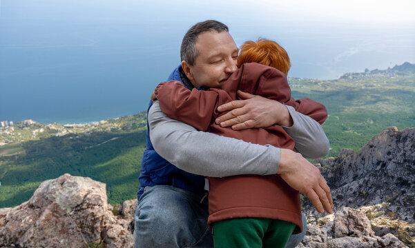 A father hugs his son on a rocky mountain peak