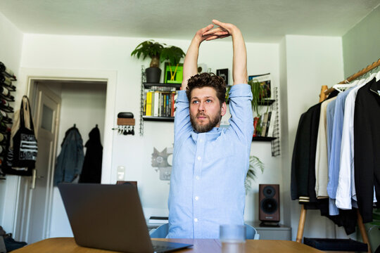 Man stretches arms during a break from remote work in home office