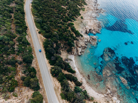 A blue car navigates a coastal road near the turquoise sea