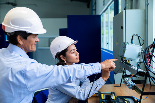 Mentor and apprentice examine electrical panel in indoor workshop