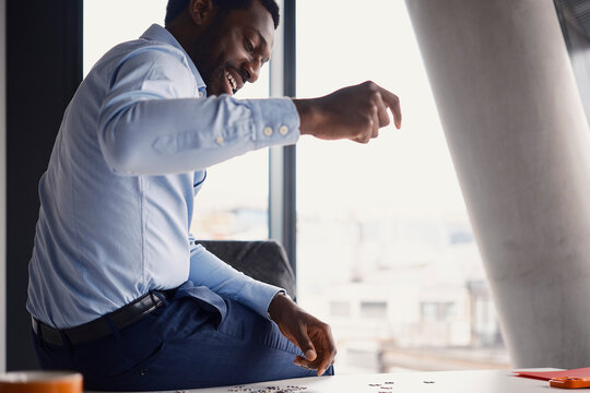 Smiling businessman drops a jigsaw puzzle piece on an office desk