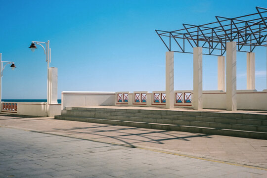 Empty seaside promenade features geometric architecture under blue sky