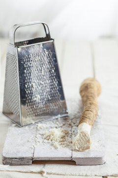 Grated horseraddish and grater on kitchen board
