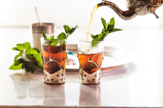Pouring black tea into traditional North African tea glass with fresh mint leaves