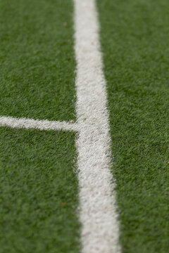 Shallow depth-of-field close-up showing a crisp white painted line crossing textured green artificial turf. Visible turf fibers create soft bokeh toward the