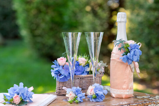 Close-up of a Bottle of champagne and two champagne flutes on a garden table with hydrangea and rose floral decorations on a summer day