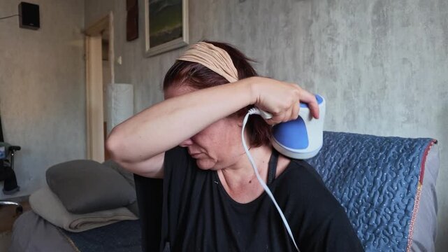 Woman Using Electric Massager on Shoulders While Sitting on Couch