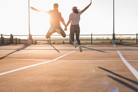 Carefree young couple jumping on parking levelat sunset