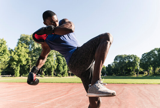 Young Afro-American man training boxing on sports field, outdoors