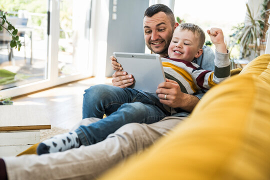 Excited father and son use a tablet on the sofa