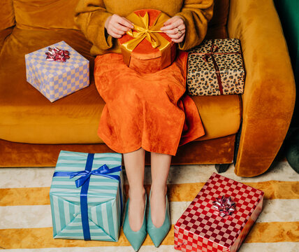 Woman sits on a brown couch unwrapping a festive holiday gift