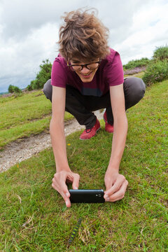 A teenage boy photographs a caterpillar with a smartphone in a park