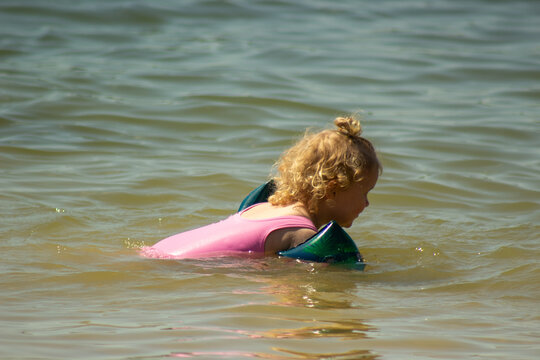 Little child swimming in river water wearing armbands closeup. Cute toddler girl in pink swimsuit swimming in sea on summer vacation for family holiday and water safety concept.