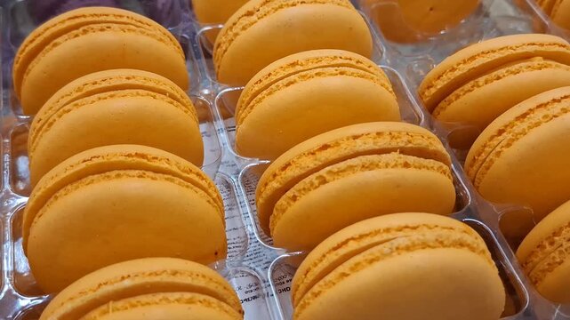 Rows of bright orange macarons arranged in a bakery display, sweet dessert, elegant treat, confectionery, food retail, colorful pastry, celebration snack.
