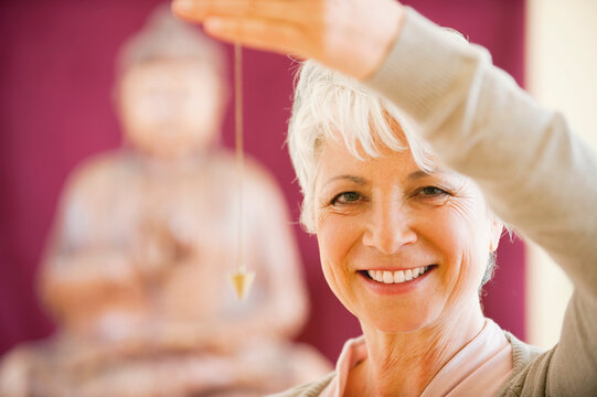 Senior woman holding pendulum, smiling, portrait