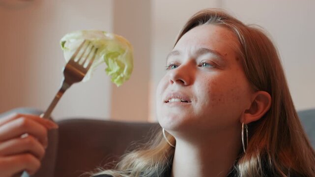 White woman examining lettuce on fork, mindful taster inhaling aroma with slight smile, savoring crisp texture in cozy interior, closeup portrait showing contentment and sensory appreciation, casual