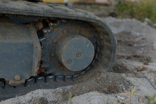 Close-up view of a heavy tracked vehicle wheel and metal tread pressing into soft mud and sand, with dirt buildup, worn mechanical parts, and an outdoor