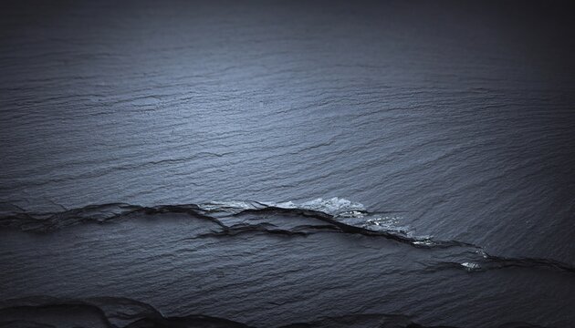 A closeup of dark grey textured slate rock featuring a prominent horizontal crack with crystalline accents