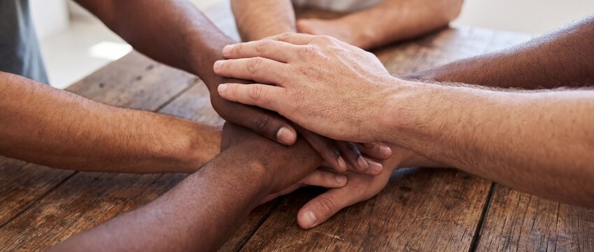 Diverse group of hands stacked together symbolizing unity and teamwork in a collaborative setting with multiple hands different skin tones layered top each other wooden table