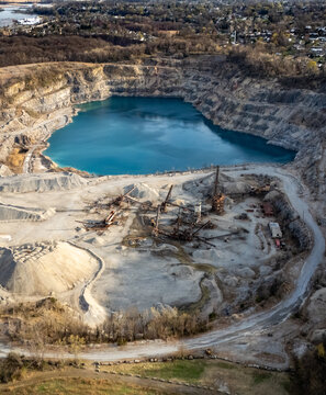 Aerial view of the Tompkins Cove Quarry featuring a deep blue water-filled pit, industrial mining equipment, gravel piles, and surrounding forest in Stony Point, New York, United States.
