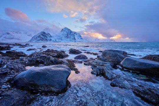 Beach of Norwegian sea on rocky coast in fjord at sunset in winter. Vareid beach, Lofoten islands, Norway, with mountains