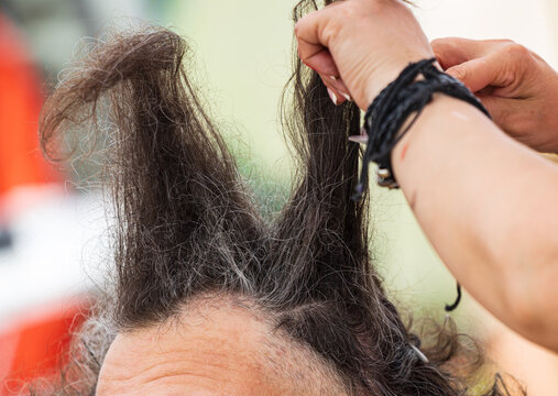 Hands gently part dark, tangled hair near scalp