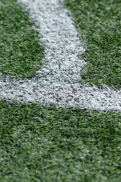 Tight close-up view of a white painted corner marking on textured green artificial grass, showing individual synthetic fibers, paint coverage, and subtle