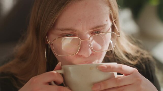 Caucasian barista tasting latte closeup, focused evaluation of aroma and crema, subtle grimace and thoughtful reaction, concentrated expression with glasses and indoor greenery, sensory quality test