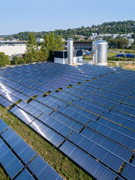 Aerial view of a solar thermic plant with rows of solar panels and large metal storage tanks in a rural landscape in Germany.