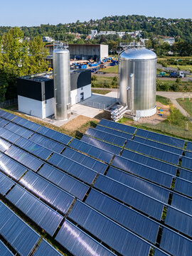 Aerial view of a solar thermal plant with large metal storage tanks and rows of solar thermal collectors in Germany.