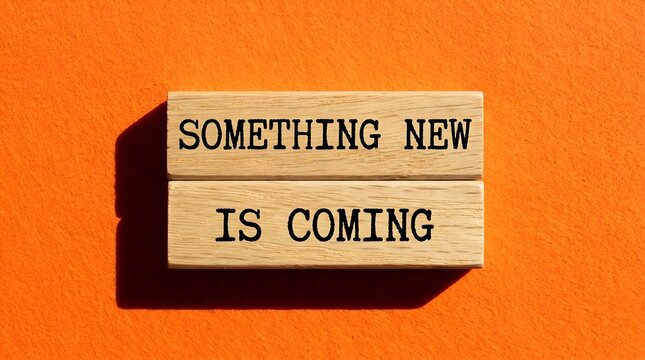 Wooden blocks with text something new is coming displayed, resting on a flat vibrant orange background representing upcoming changes and future growth