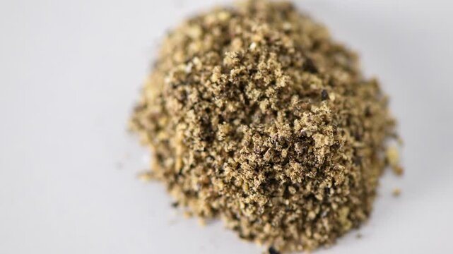 Small pile of whole black peppercorns on white background

