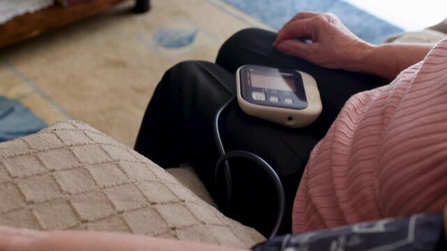 Elderly woman at home checking her blood pressure with a monitor. Ideal for health, medical care, and home assistance concepts