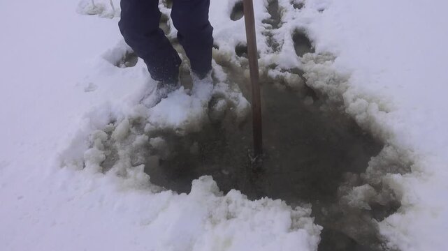 Unreliable so-called rotten ice, spring sludge under a layer of snow on the lake. A man measures the depth of a lake with a pole