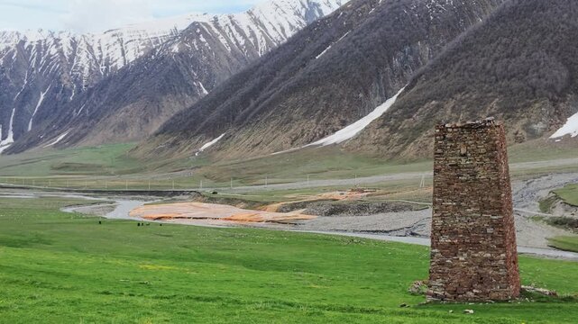 Ancient stone defensive watchtower standing in a lush alpine valley with snowy mountain peaks in the background, heritage site, travel, tourism, historical architecture at Truso valley, Georgia