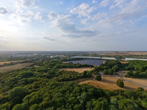 Aerial view of a solar farm nestled among lush green forests and open fields under a bright sky in Irchester, England, United Kingdom.