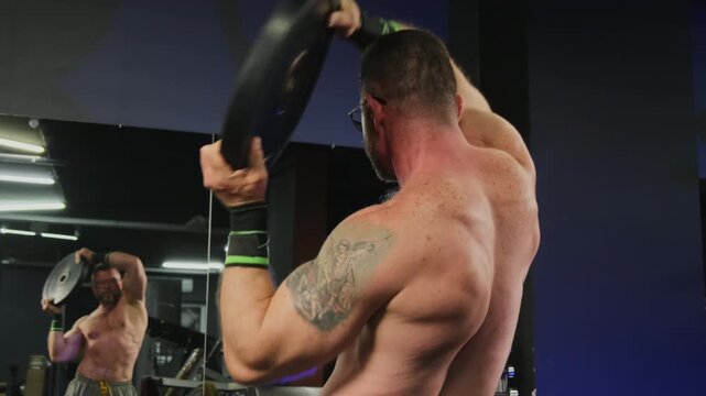Disciplined bodybuilder performs circular movements with heavy plate. Powerful athlete develops greater upper-body stability and endurance