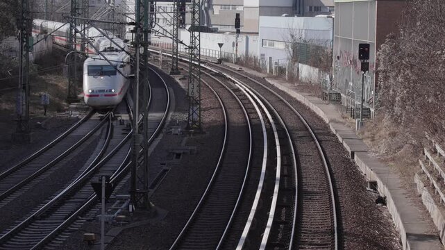 Train tracks An elevated view captures multiple railway tracks with overhead catenary lines curving through an urban industrial area during daytime. In the distance, a white high-speed passenger train