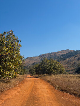Red dirt road leading toward a rocky mountain under a clear blue sky, Eswatini, Southern Africa