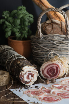 Close-up of Pancetta Arrolotata with slices of pancetta, fresh bread bread and a basil plant on a wooden table