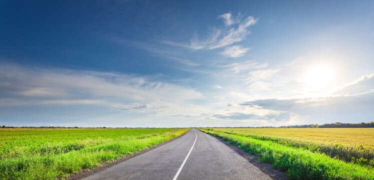 Asphalt road stretches wide through vibrant green fields