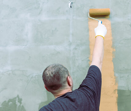 Man applies fresh paint with a roller on a bare wall