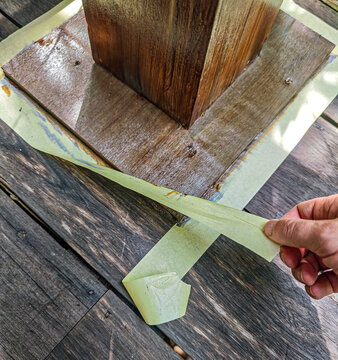 Hand peels away tape from wet wooden surface